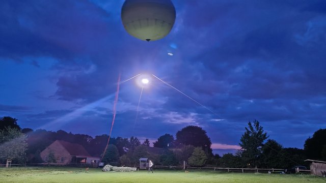 Ein großer Ballon schwebt über einer grünen Wiese. Vom Ballon strahlt ein helles Licht und beleuchtet die Wiese.