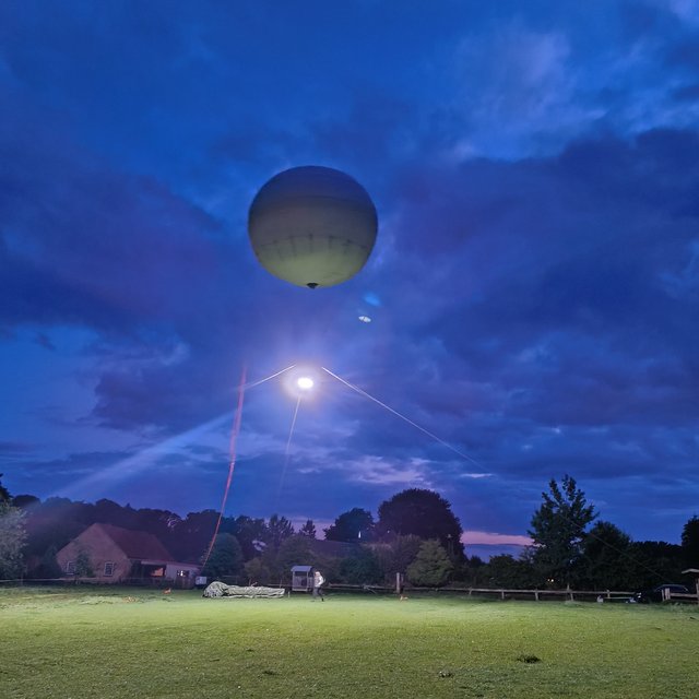 A large balloon floats above a green meadow. A bright light shines from the balloon, illuminating the meadow.