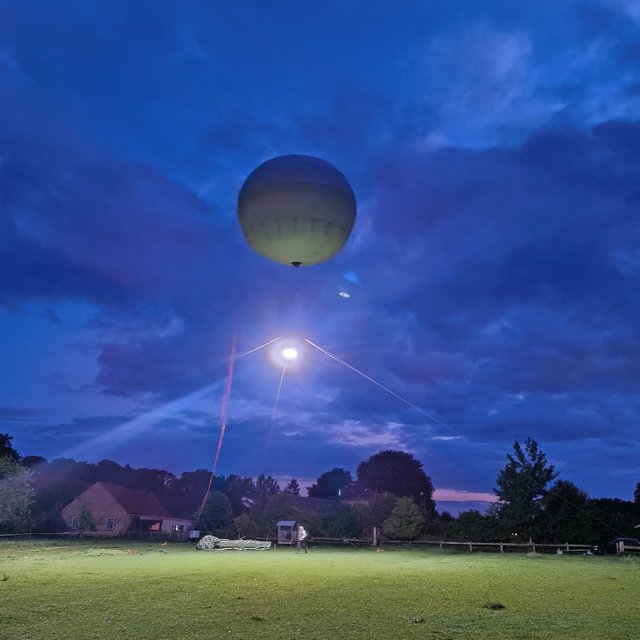 Ein großer Ballon schwebt über einer grünen Wiese. Vom Ballon strahlt ein helles Licht und beleuchtet die Wiese.