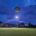 A large balloon floats above a green meadow. A bright light shines from the balloon, illuminating the meadow.